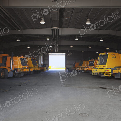 Snow ploughs and maintenance vehicles in a garage at an airport.