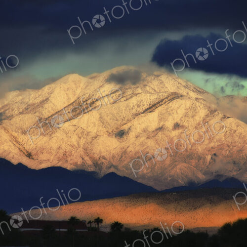 Snowcovered slopes of a mountain range with a dark stormy sky above, and a low sunlit… Snowcovered slopes of a mountain range with a dark stormy sky above, and a low sunlit…