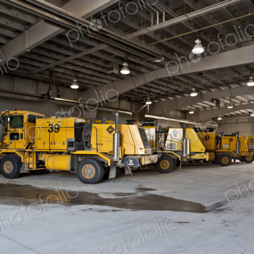 Snowploughs and airport vehicles parked in a large shed.