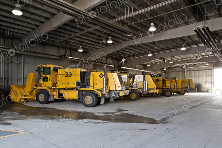 Snowploughs and airport vehicles parked in a large shed.