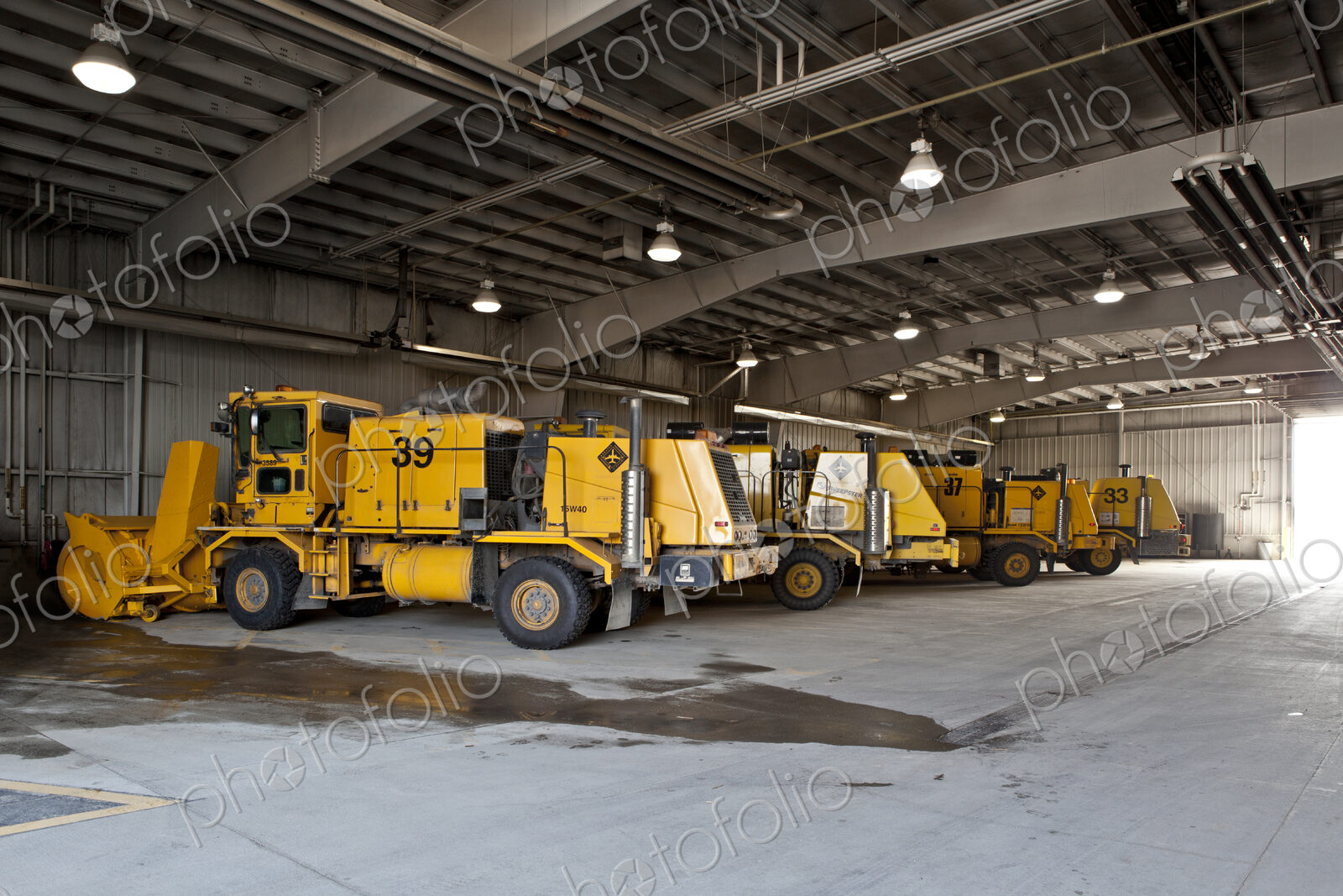 Snowploughs and airport vehicles parked in a large shed.