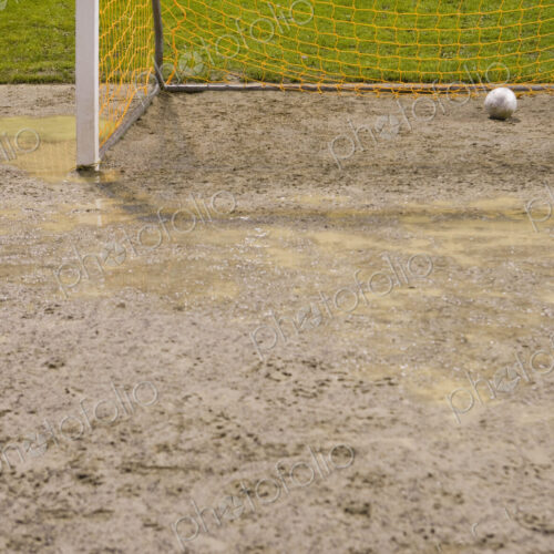 Soccer ball in goal net on muddy soccer field.