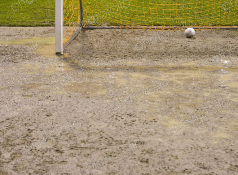 Soccer ball in goal net on muddy soccer field.