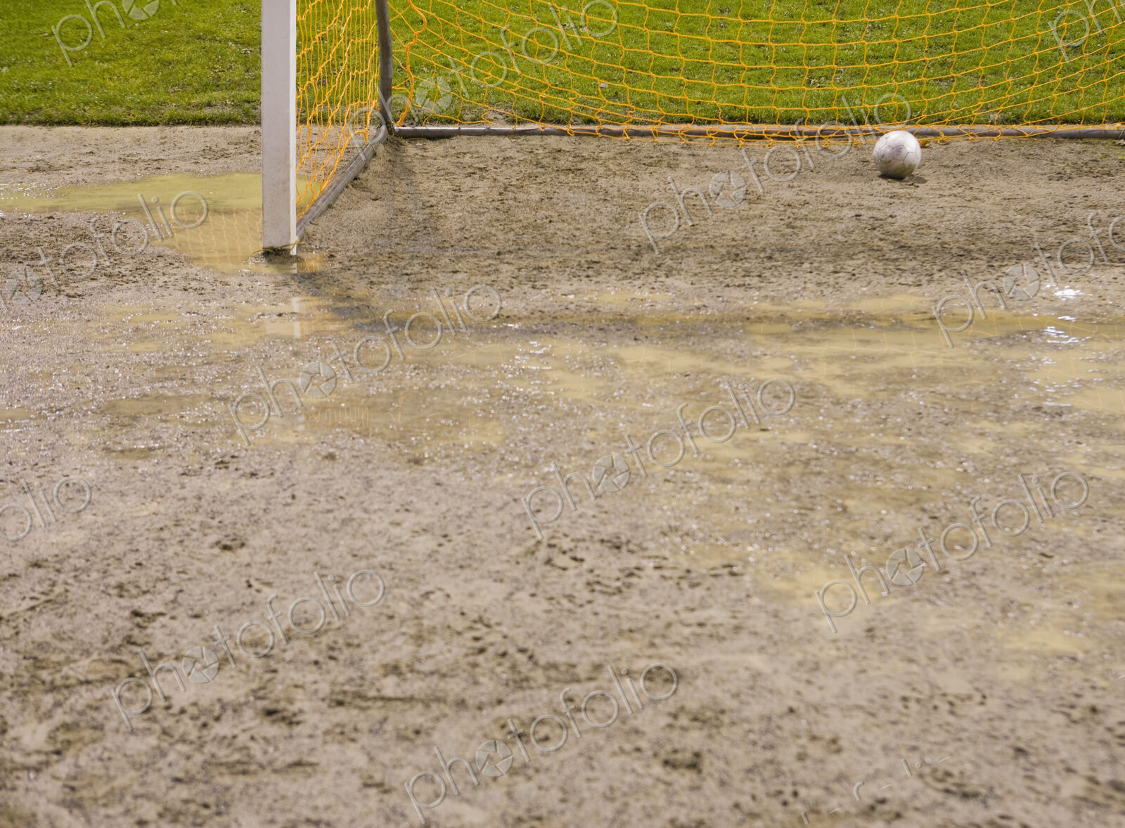 Soccer ball in goal net on muddy soccer field.