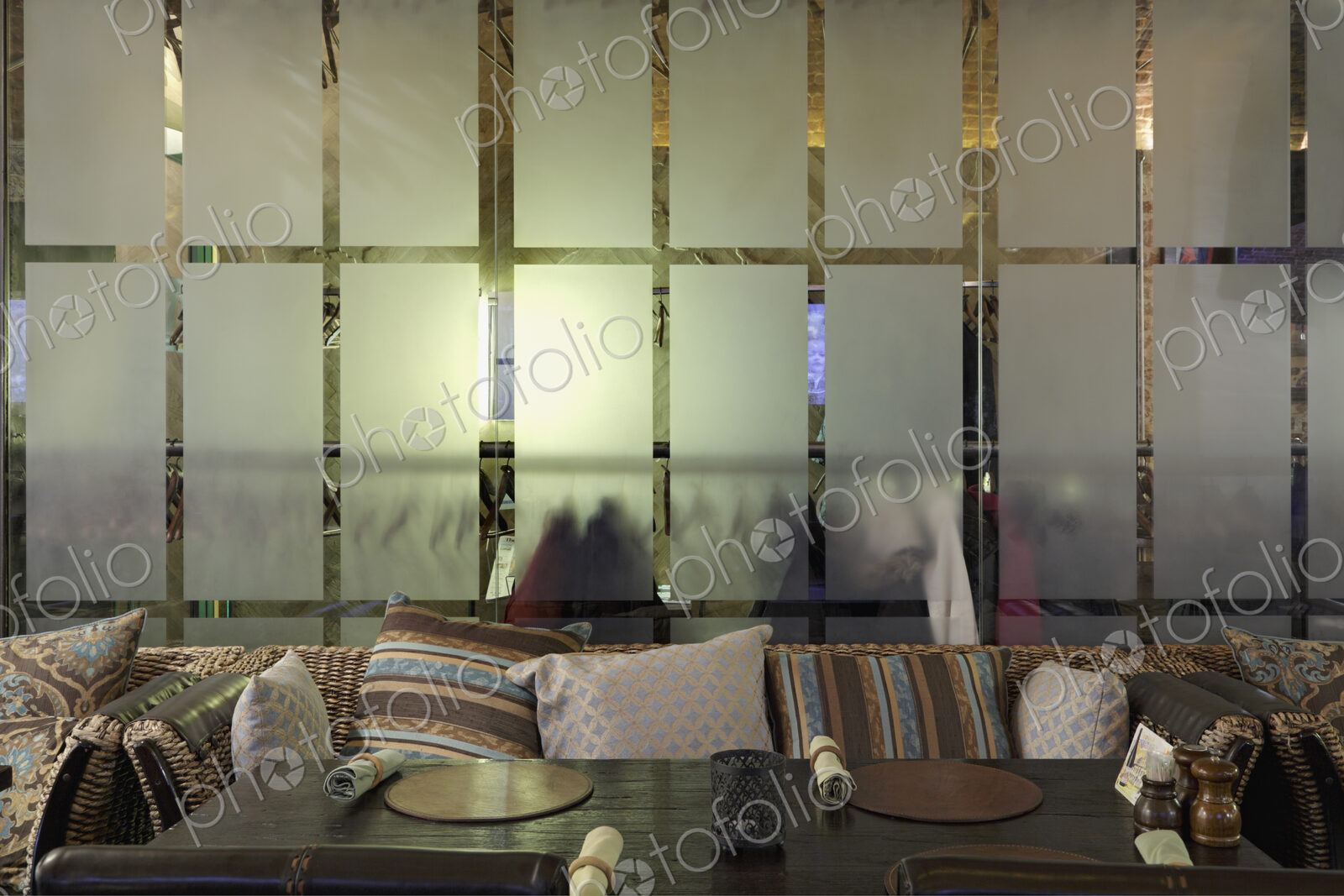 Sofa with many pillows against glass wall in restaurant.