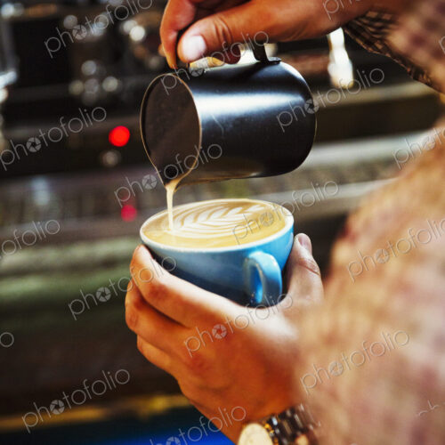 Specialist coffee shop. A barista pouring hot milk in to the froth on a cup of coffee… Specialist coffee shop. A barista pouring hot milk in to the froth on a cup of coffee…