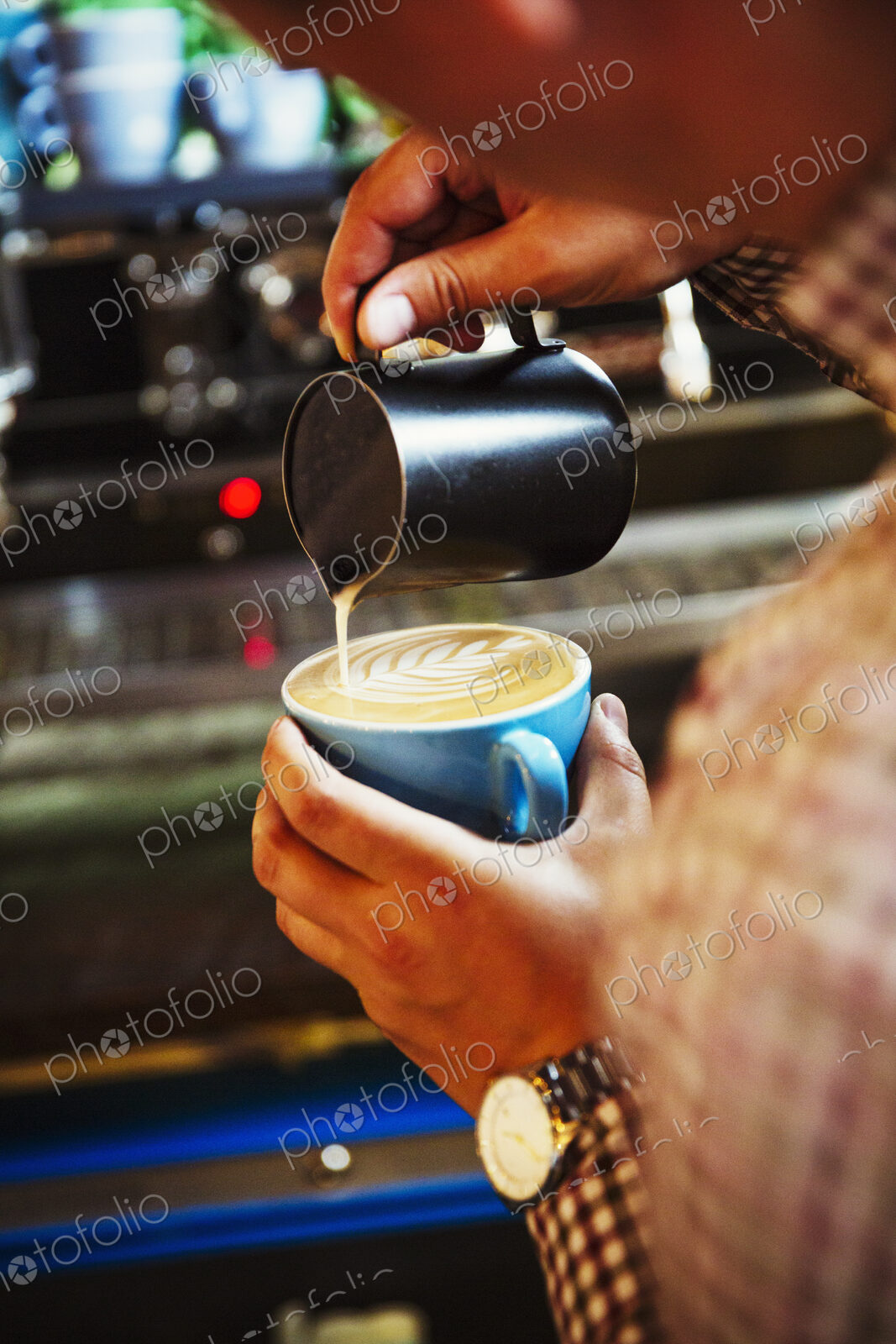 Specialist coffee shop. A barista pouring hot milk in to the froth on a cup of coffee…