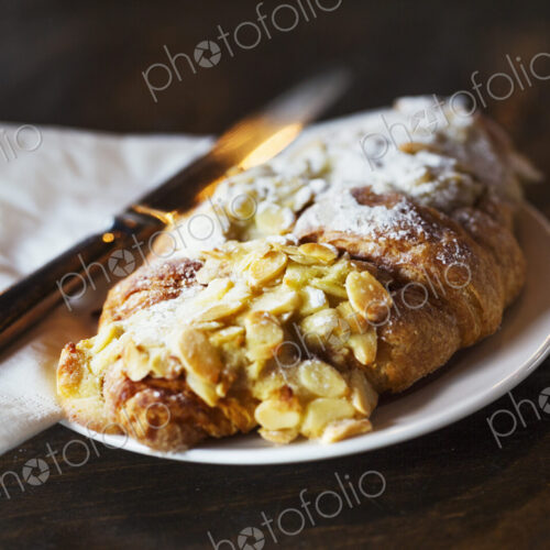 Specialist coffee shop. A fresh pastry, an almond croissant on a place with a knife. Specialist coffee shop. A fresh pastry, an almond croissant on a place with a knife.