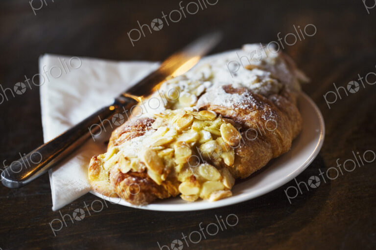Specialist coffee shop. A fresh pastry, an almond croissant on a place with a knife.