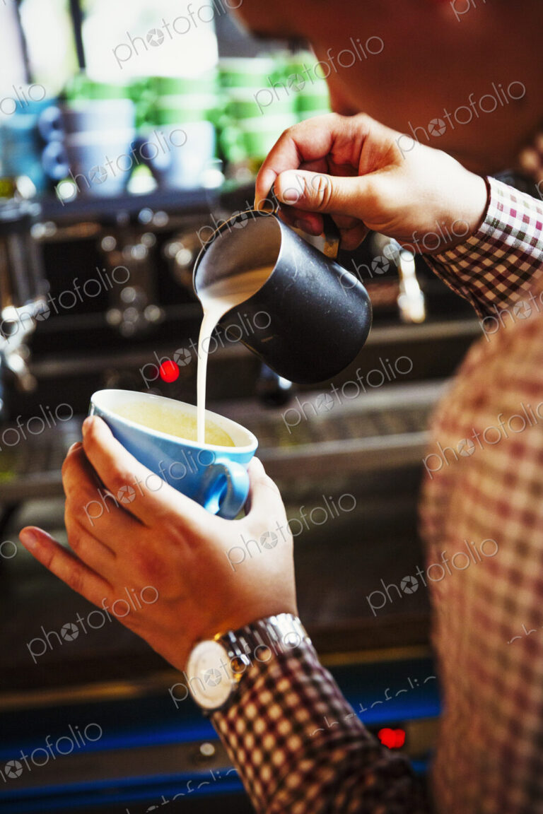 Specialist coffee shop. A person making coffee and pouring milk into a cup held at an…