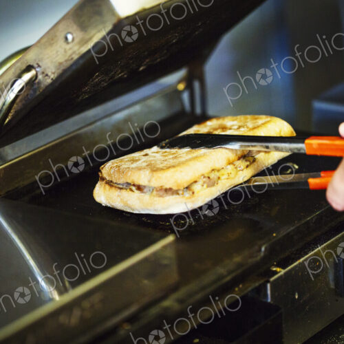 Specialist coffee shop. A person preparing a toasted sandwich at a grill. Specialist coffee shop. A person preparing a toasted sandwich at a grill.