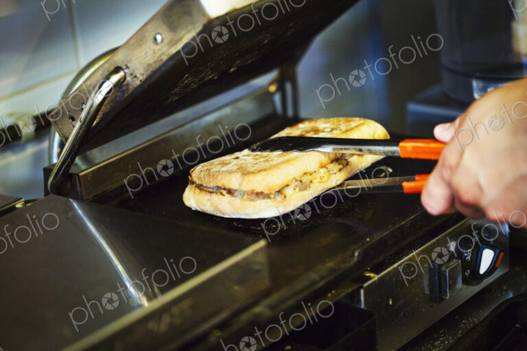 Specialist coffee shop. A person preparing a toasted sandwich at a grill.