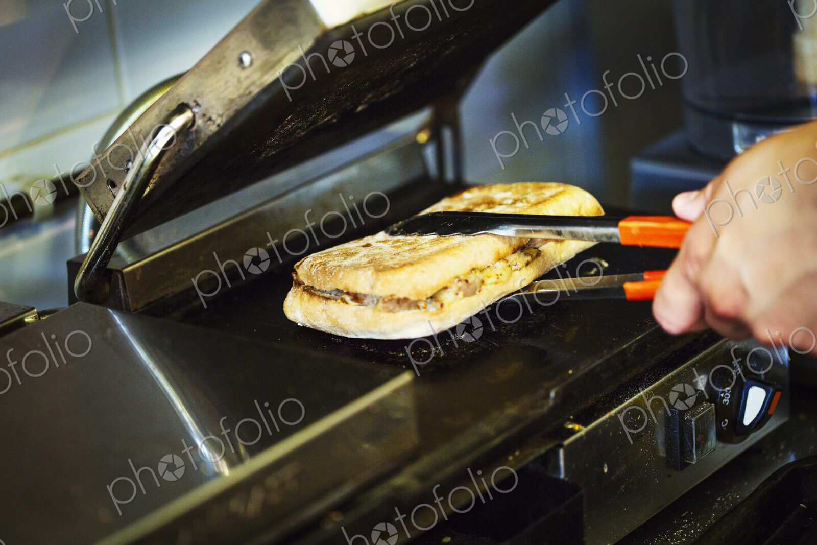 Specialist coffee shop. A person preparing a toasted sandwich at a grill.