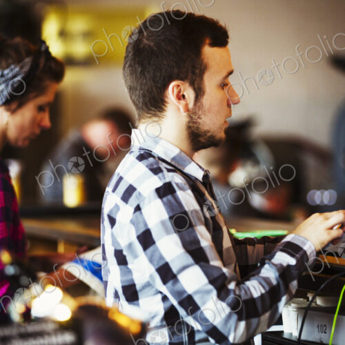 Specialist coffee shop. A woman and man working behind the counter by a roasting machine. Specialist coffee shop. A woman and man working behind the counter by a roasting machine.