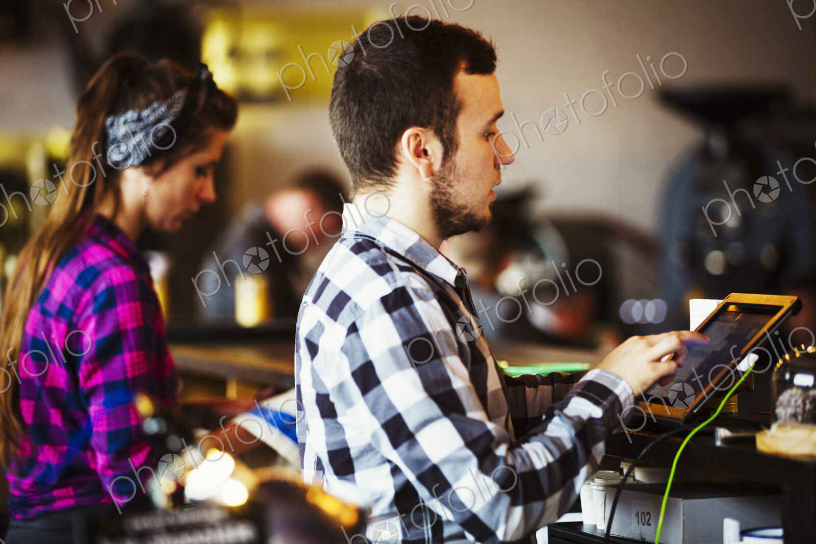 Specialist coffee shop. A woman and man working behind the counter by a roasting machine.