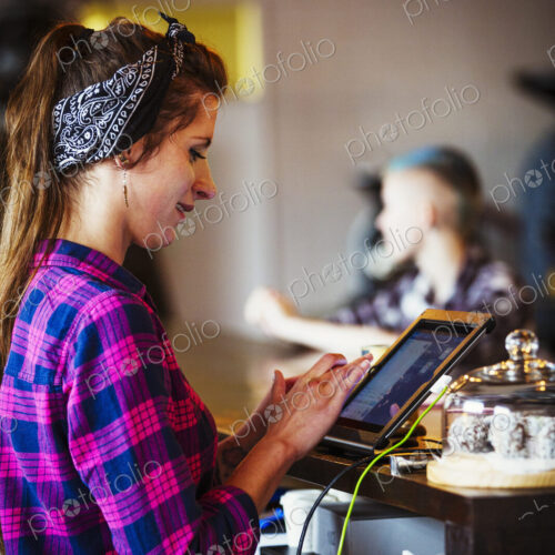 Specialist coffee shop. A woman working behind the counter using the touch screen on… Specialist coffee shop. A woman working behind the counter using the touch screen on…