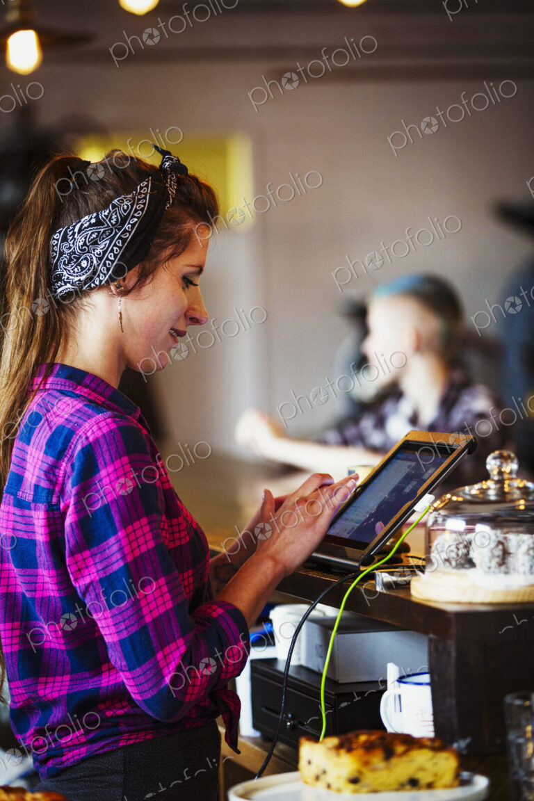Specialist coffee shop. A woman working behind the counter using the touch screen on…