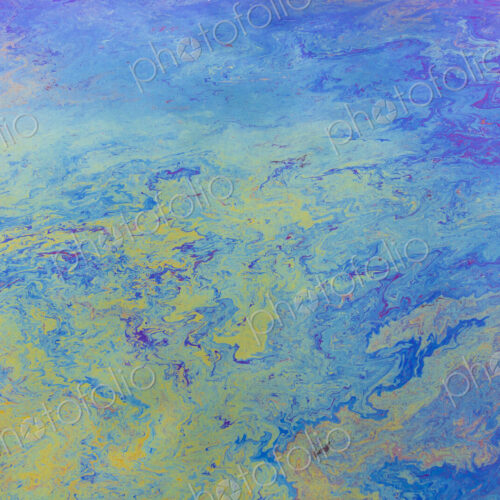 Spilled diesel fuel on surface on ocean water, close up, blue and yellow patterns.