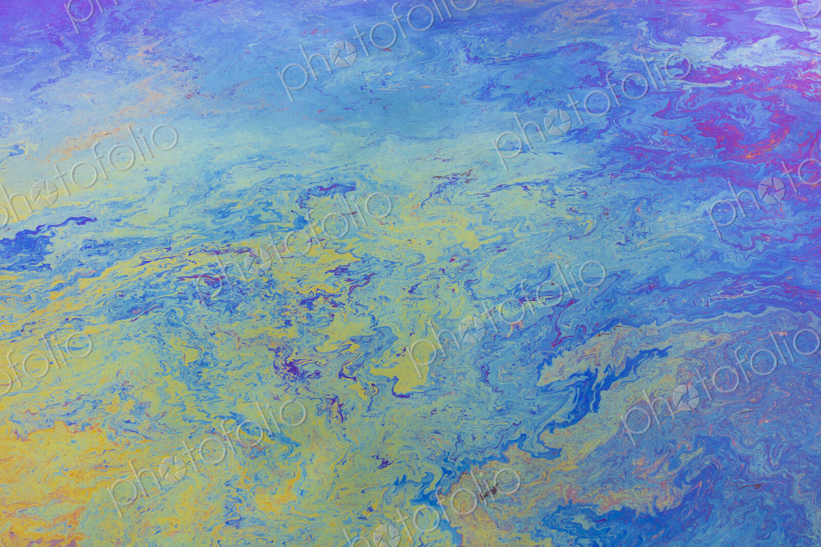 Spilled diesel fuel on surface on ocean water, close up, blue and yellow patterns.