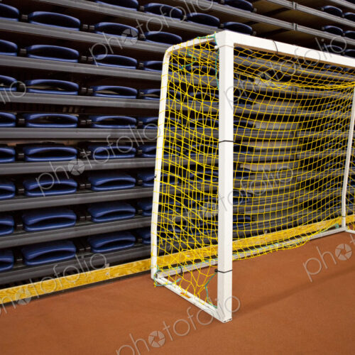 Stack of folded seats at an indoor sports venue, and a practise football goal net.