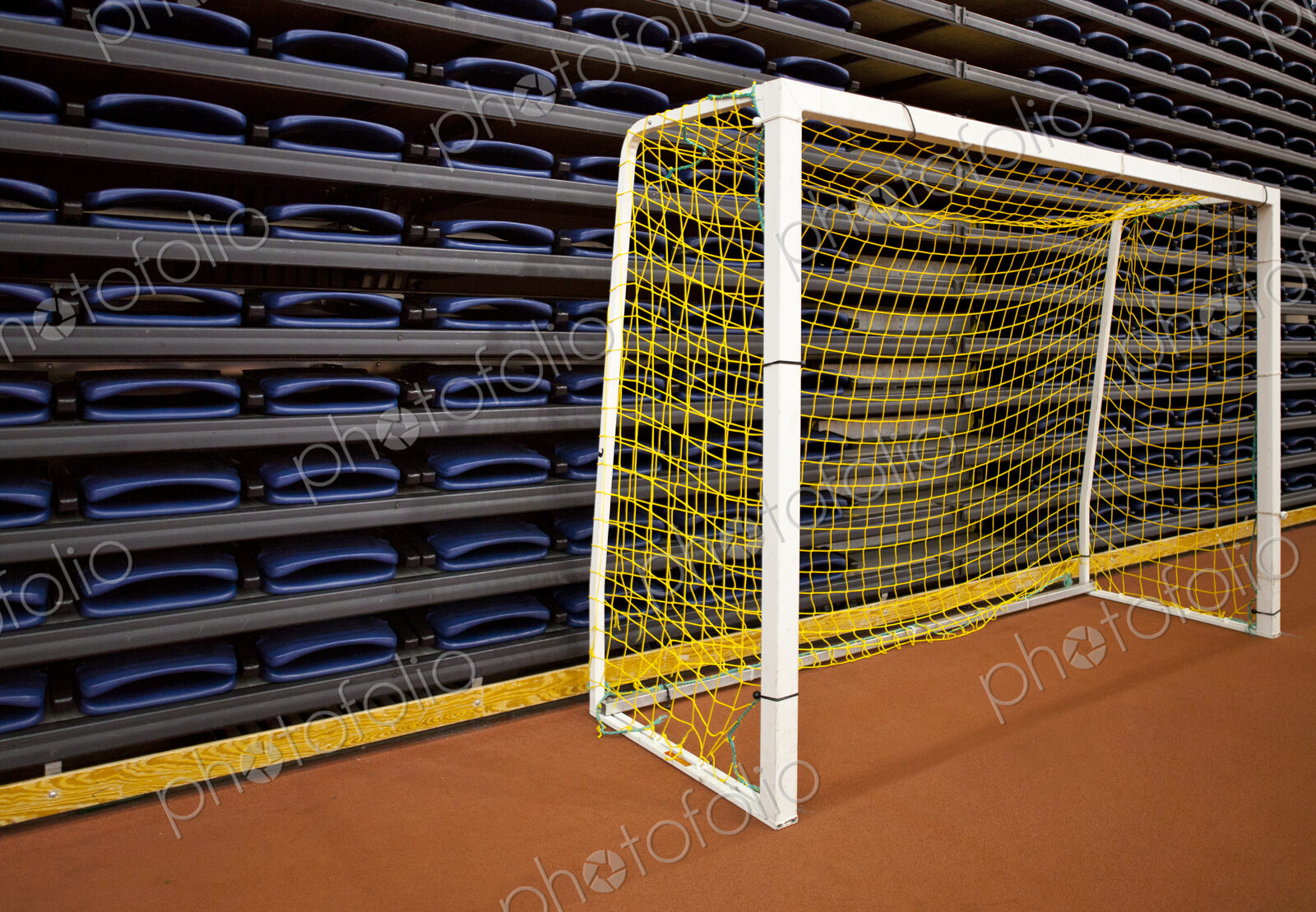 Stack of folded seats at an indoor sports venue, and a practise football goal net.