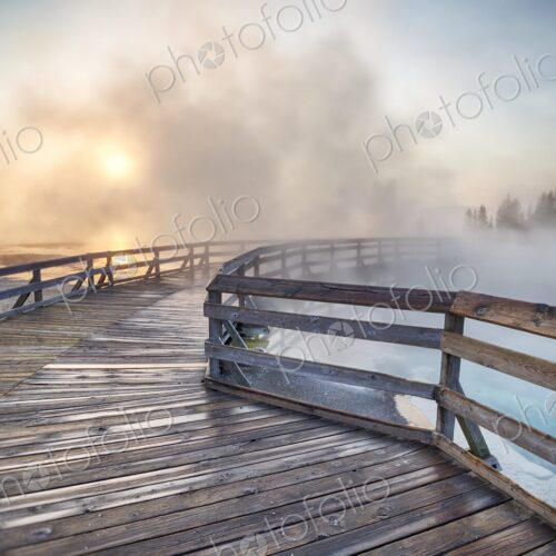 Steaming hot spring at sunrise with wooden boardwalk curving through West Thumb Geyser… Steaming hot spring at sunrise with wooden boardwalk curving through West Thumb Geyser…