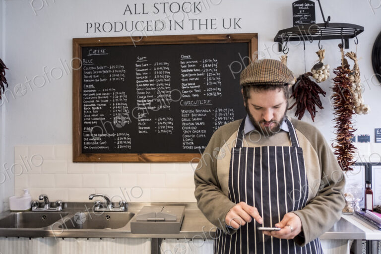 Store owner in a delicatessen using a digital tablet.