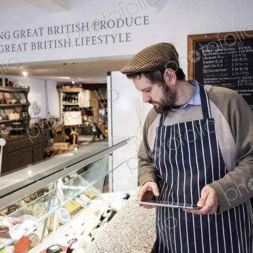 Store owner in a delicatessen using a digital tablet. Store owner in a delicatessen using a digital tablet.