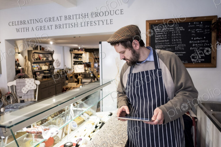 Store owner in a delicatessen using a digital tablet.