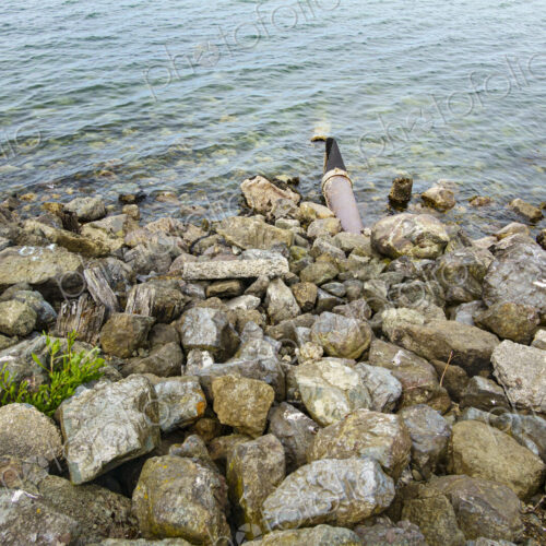 Storm sewer outlet, a pipe hidden under rocks discharging effluents and sewage into… Storm sewer outlet, a pipe hidden under rocks discharging effluents and sewage into…