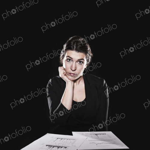 Studio portrait, a woman sitting with paperwork spread out and her hand on her chin,… Studio portrait, a woman sitting with paperwork spread out and her hand on her chin,…