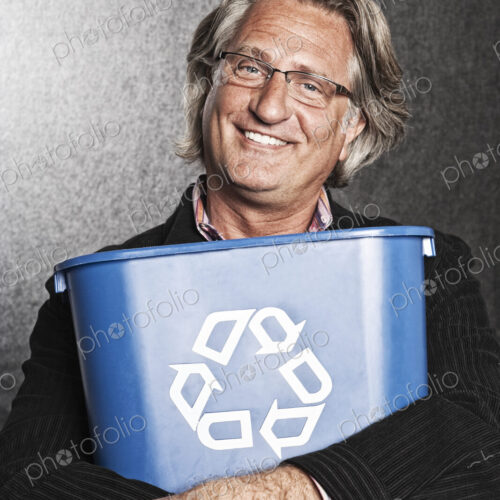 Studio portrait of caucasian man actor holding a blue recycling bin to his chest.