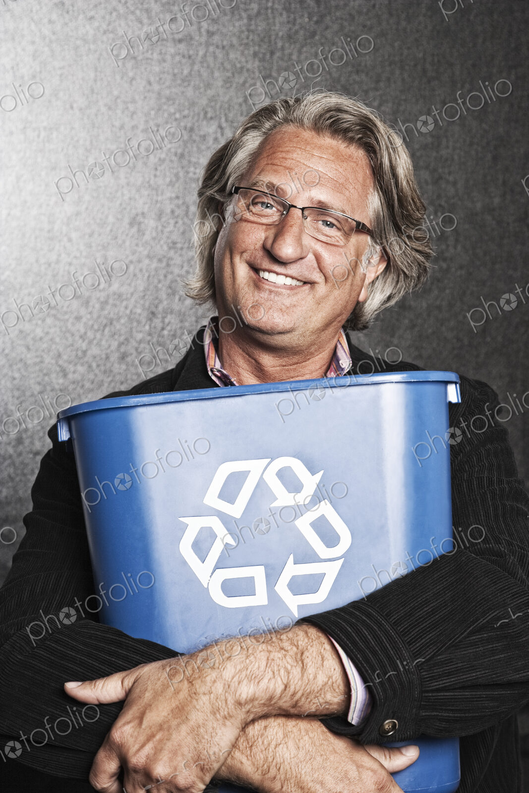Studio portrait of caucasian man actor holding a blue recycling bin to his chest.