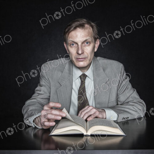 Studio portrait of caucasian man actor seated reading from an open book. Studio portrait of caucasian man actor seated reading from an open book.