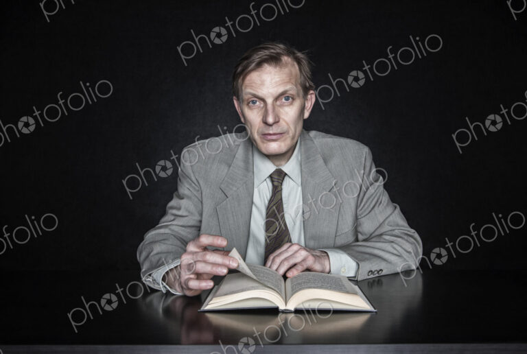 Studio portrait of caucasian man actor seated reading from an open book.