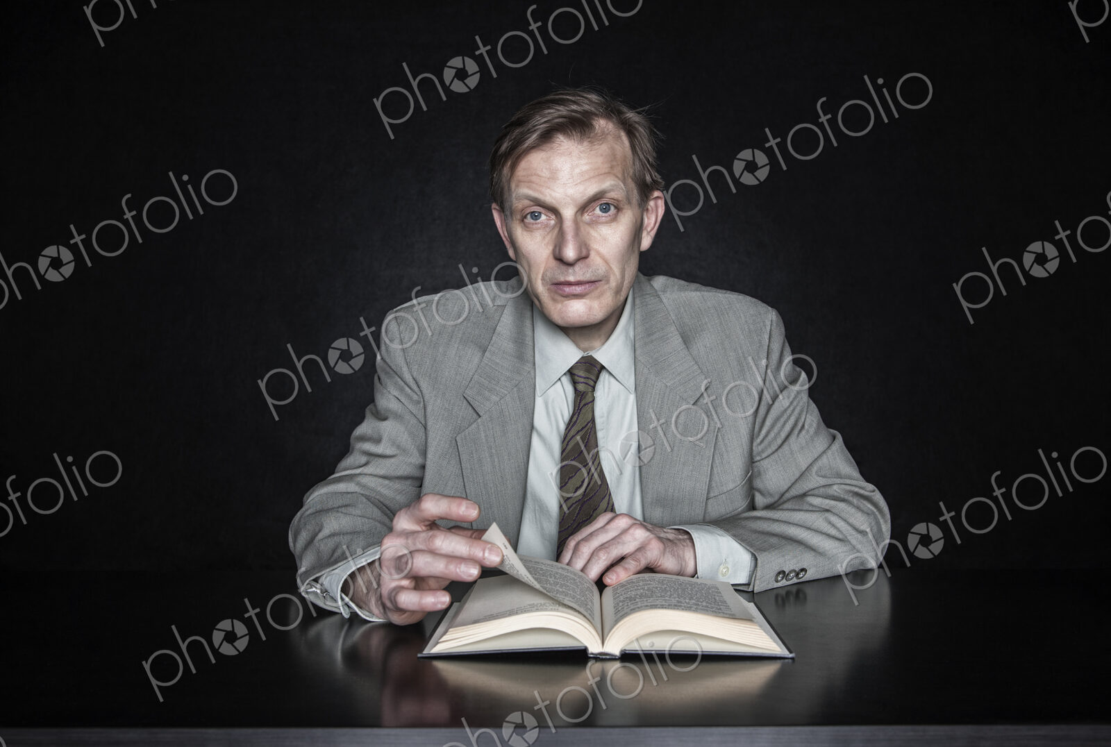 Studio portrait of caucasian man actor seated reading from an open book.