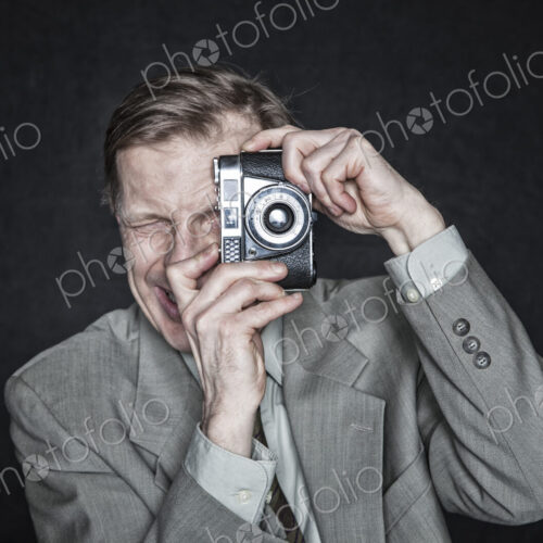 Studio portrait of caucasian man actor using a camera, squinting and focussing.