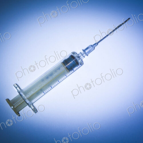 Studio shot of a plastic syringe with needle and plunger on a blue background
