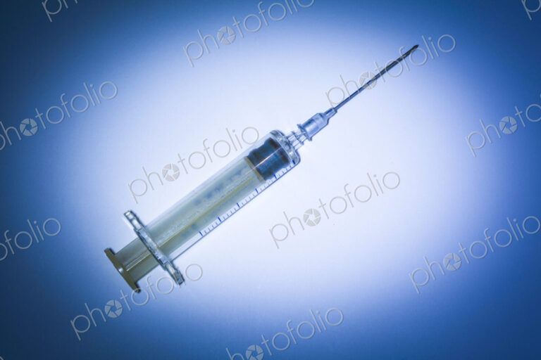 Studio shot of a plastic syringe with needle and plunger on a blue background