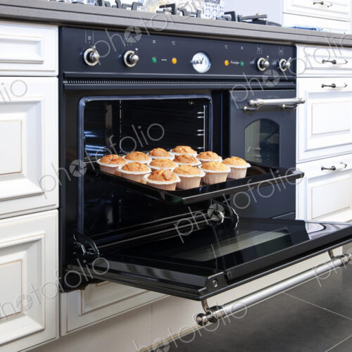Stylish oven in a modern kitchen, door open with fresh baked cup cakes on a baking tray. Stylish oven in a modern kitchen, door open with fresh baked cup cakes on a baking tray.