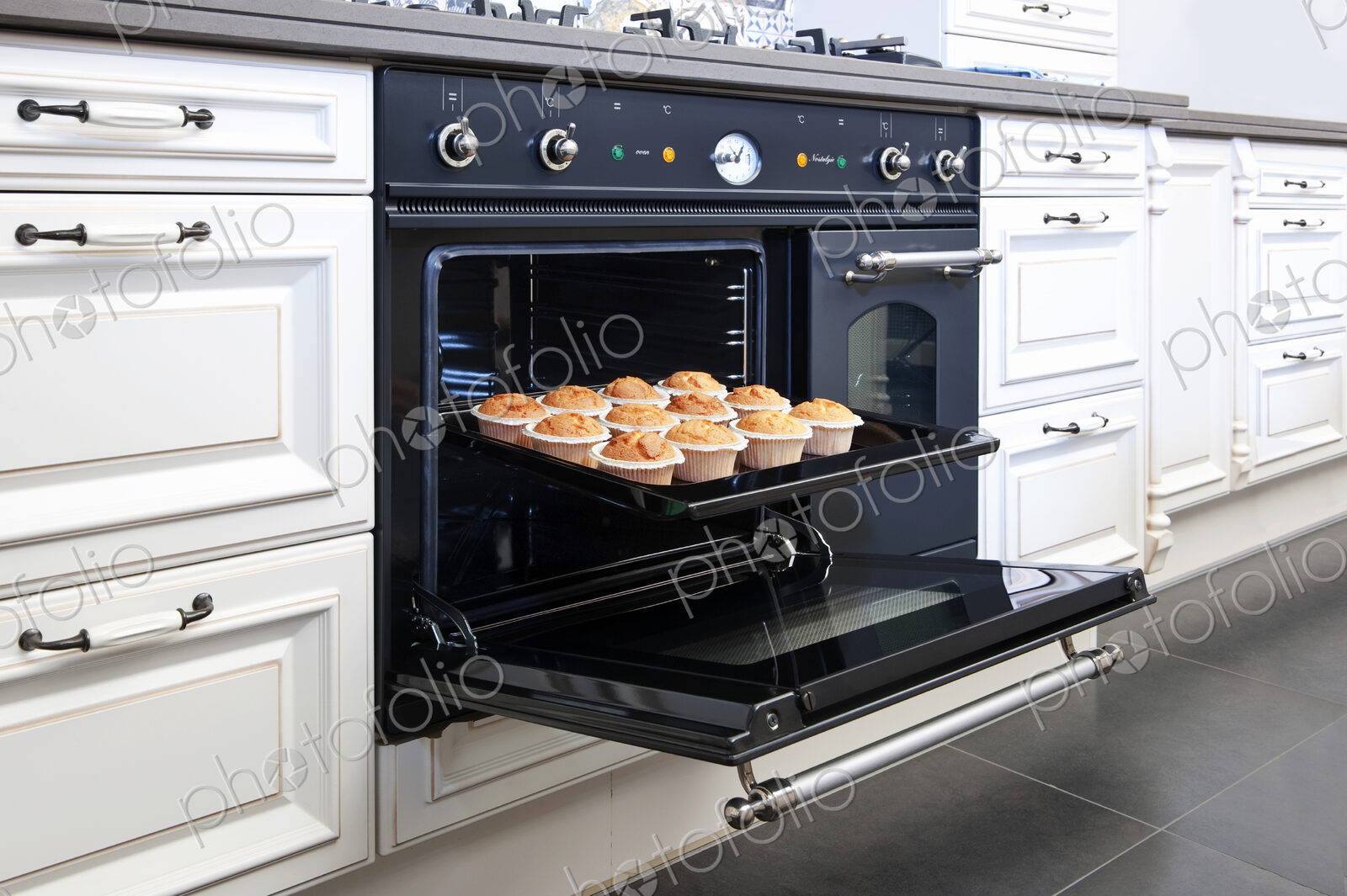 Stylish oven in a modern kitchen, door open with fresh baked cup cakes on a baking tray.