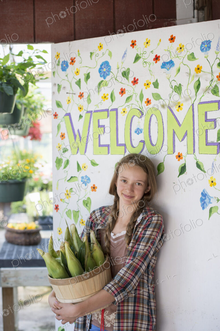Summer on an organic farm. A girl holding a basket of fresh corn standing by the…