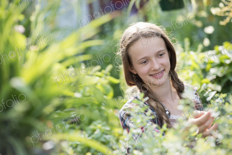 Summer on an organic farm. A young girl in a plant nursery full of flowers.
