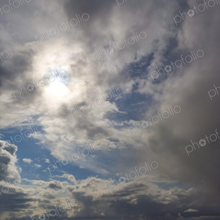 Sun behind grey clouds and glimpses of blue sky,