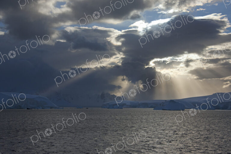 Sun breaking through the storm clouds hitting the icebergs along the west coast of the…
