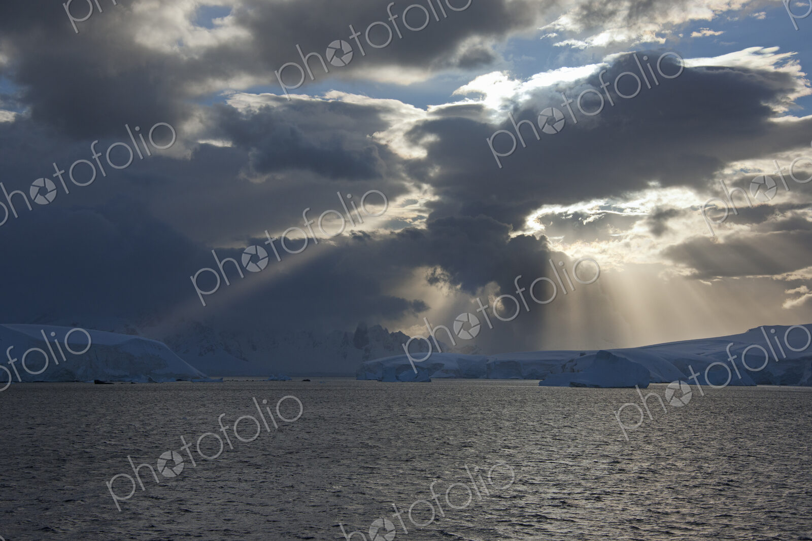 Sun breaking through the storm clouds hitting the icebergs along the west coast of the…