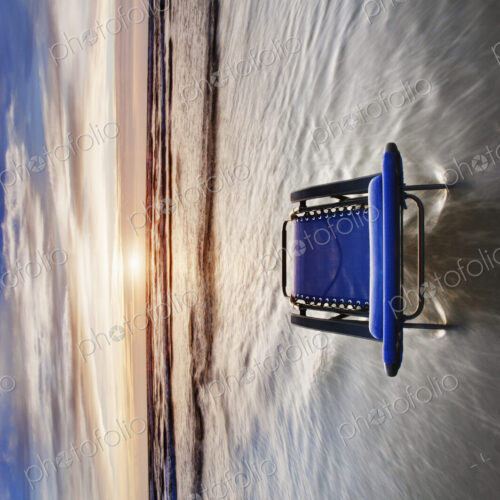 Sun lounger in shallow wave at beach at sunset.