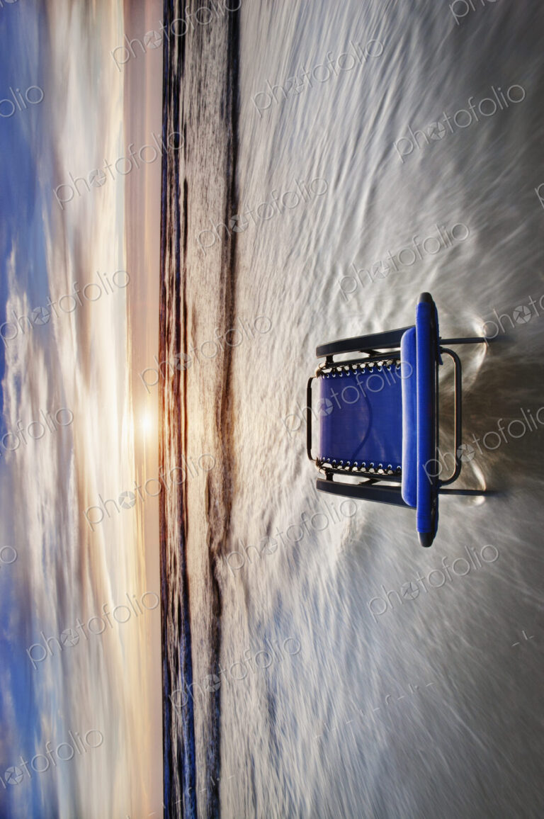Sun lounger in shallow wave at beach at sunset.