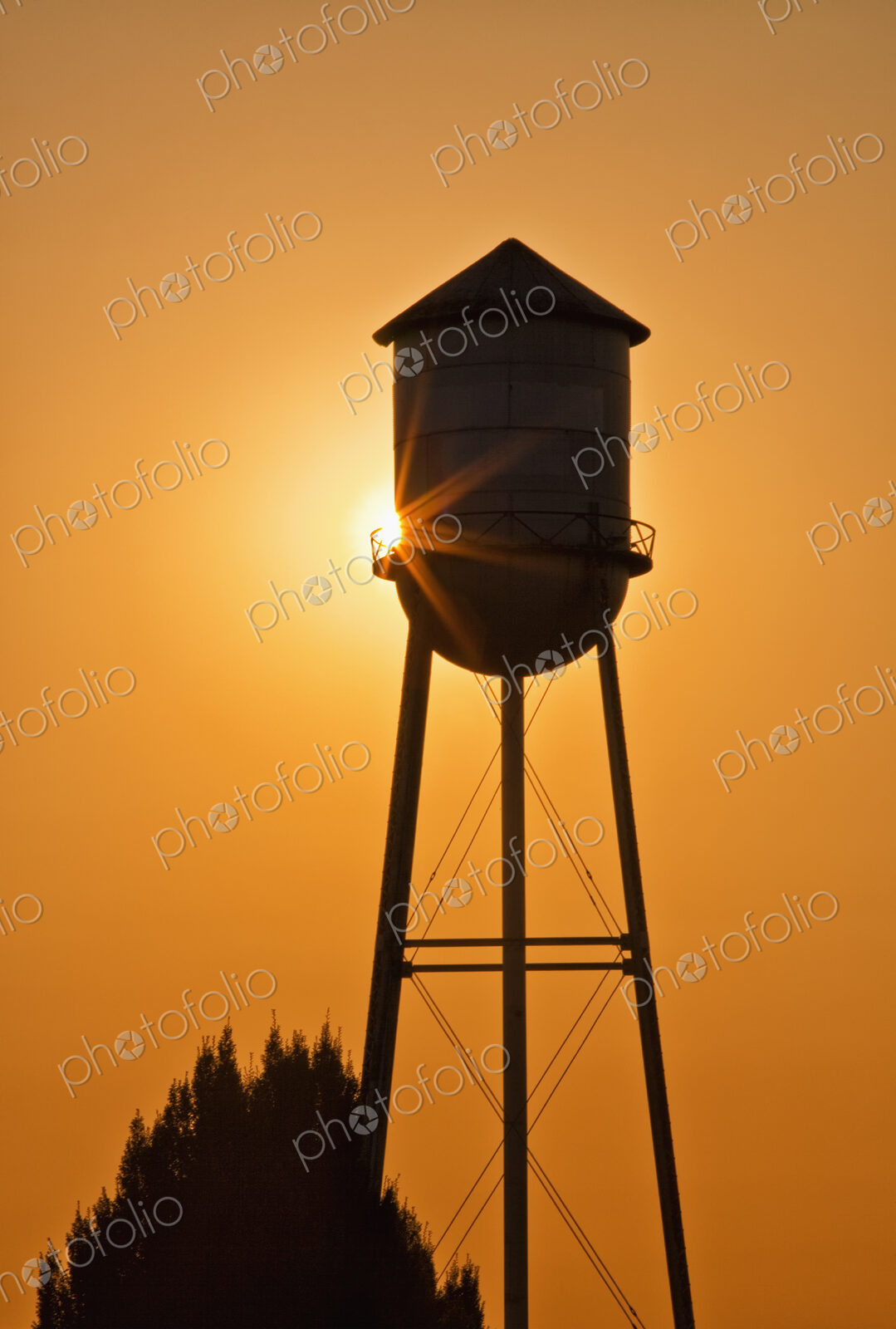Sun setting behind agricultural water tower.