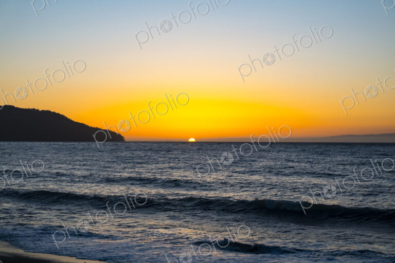 Sun setting on the horizon above the Strait of Juan de Fuca over the sea.